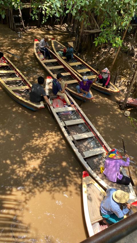       Small wooden sampans with passengers glide through a narrow, tree-shaded canal of the Mekong Delta.
  