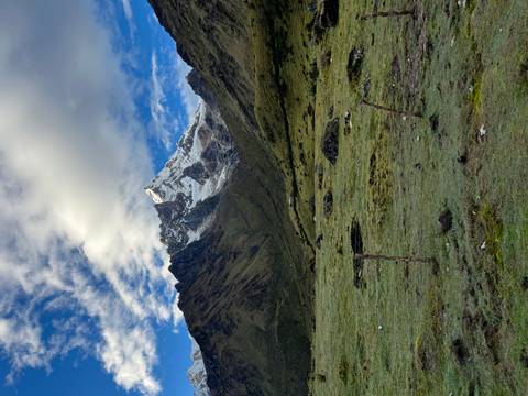       Snow-clad Salkantay peak rising above grassy plain under dramatic cloud pattern.
  