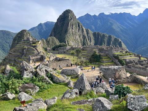       Panoramic view of Machu Picchu terraces and peak with visitors exploring.
  
