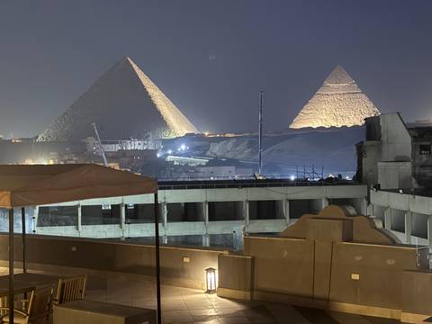       Nighttime view of the illuminated Great Pyramids of Giza rising behind urban rooftops.
  