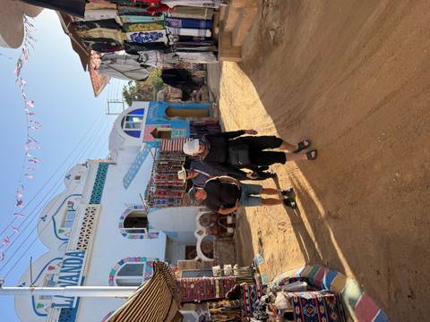       Travelers stroll through a colorful Nubian village street lined with handicraft shops.
  