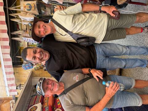       Smiling travelers pose with a friendly local vendor in a bustling market alley.
  
