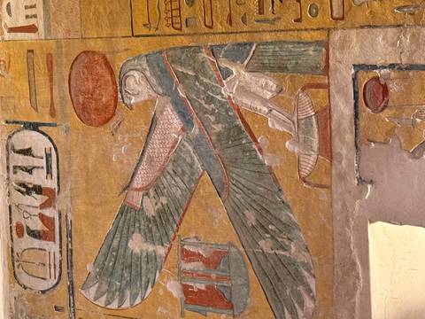       Brightly colored relief of a winged falcon-headed Egyptian deity painted on an ochre temple wall.
  