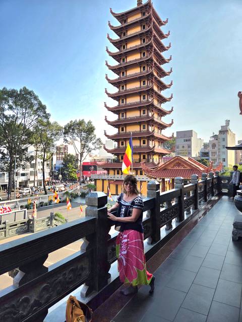       Visitor smiles on a balcony overlooking a busy street and multi-tiered yellow pagoda.
  