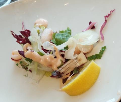       Close-up of a small plated salad with dressing and a lemon wedge, slightly out of focus.
  