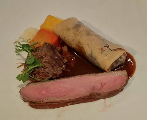       Gourmet dish featuring sliced duck, vegetable roll and rich sauce artistically arranged on a white plate.
  