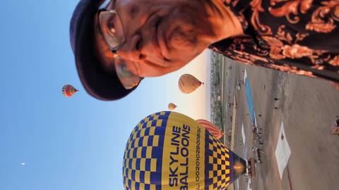       Close-up of a man on a sunrise hot-air-balloon field with colourful balloons ascending in the background.
  