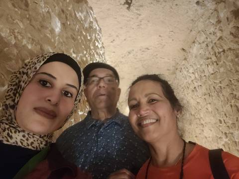       Low-light selfie of three travellers inside a stone passageway with rough walls.
  