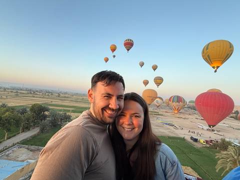       Smiling couple with dozens of colorful hot-air balloons rising over the Nile farmlands at sunrise.
  