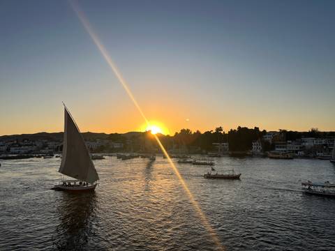       Felucca sailing on the Nile with golden sunset casting reflections on the water.
  