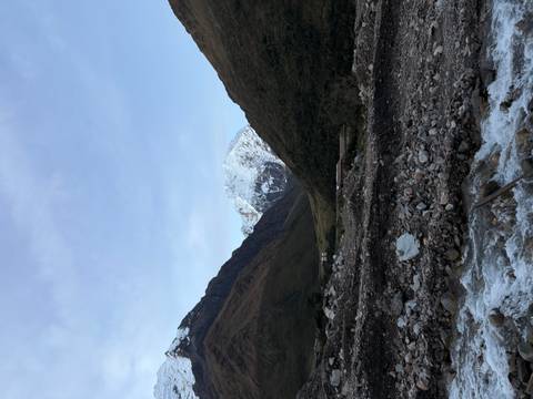       Snow-capped Andean peak towering above a V-shaped valley with a rocky river in the foreground.
  
