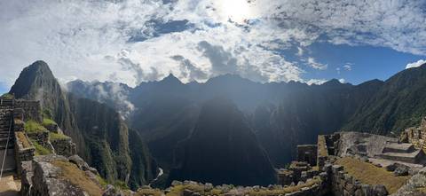      Wide panoramic shot of the lush green canyon and surrounding peaks beyond Machu Picchu ruins under dramatic skies.
  
