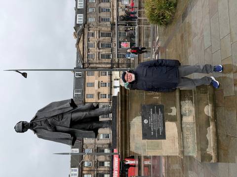       Traveller stands next to the Sherlock Holmes statue in rainy Edinburgh city square.
  