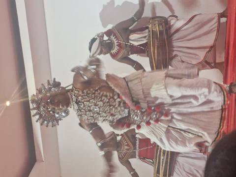       Traditional Kandyan dancers in elaborate costumes perform on an indoor stage.
  