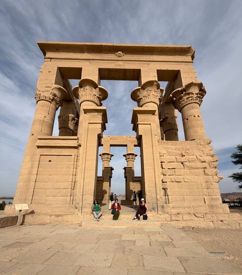       Massive sandstone columns and lintels of Philae Temple with tiny visitors for scale under hazy sky
  