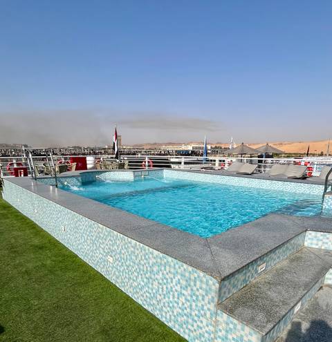       Rooftop swimming pool on a Nile cruise ship with desert hills and distant town in background
  