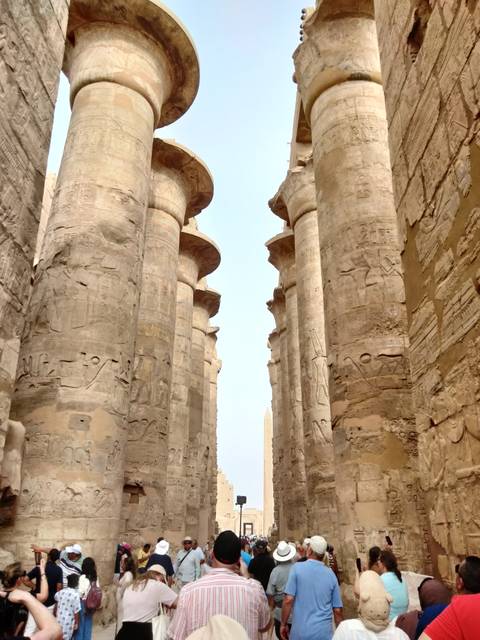       Towering carved stone columns covered in hieroglyphs framing a distant obelisk inside an ancient Egyptian temple
  