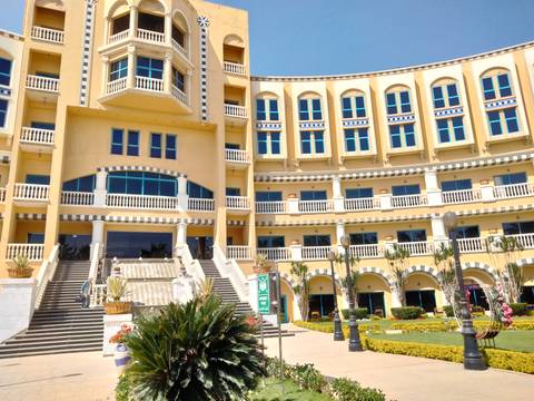       Elegant yellow-painted waterfront hotel with sweeping staircase, arched balconies and potted plants under a clear blue sky
  
