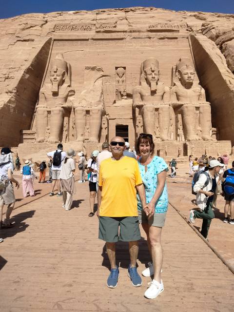       Tourists posing in front of the giant seated statues of Abu Simbel temple on a bright day
  