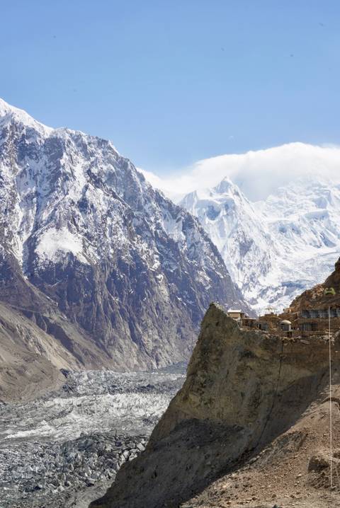       Dramatic snow-covered peaks of the Karakoram Range with a small stone settlement perched on a rocky outcrop
  
