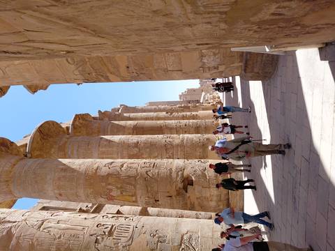       Tourists walking among gigantic hieroglyph-covered columns of Karnak Temple under a bright blue sky
  