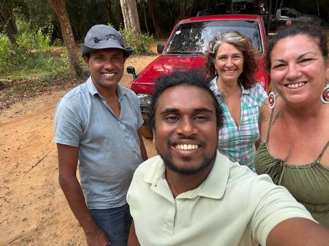       Selfie of four friends standing beside a red off-road vehicle on a dirt track in Sri Lanka
  