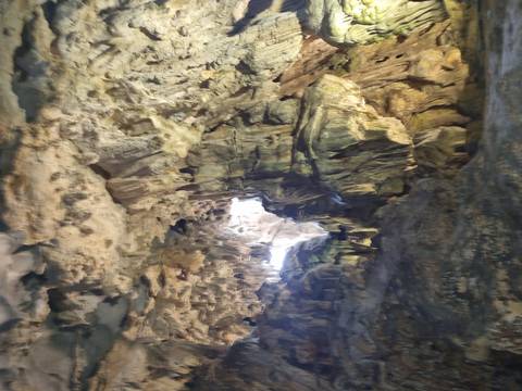       Dimly lit interior of a limestone cave with rock formations and a bright aperture overhead.
  