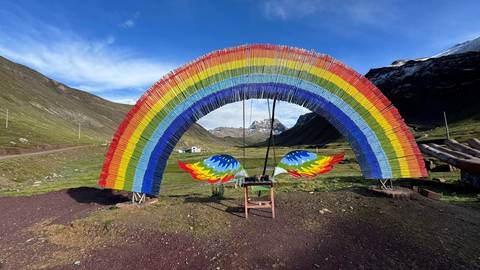       A vibrant sculptural rainbow arch frames the valley near Rainbow Mountain with snow-capped peaks beyond.
  