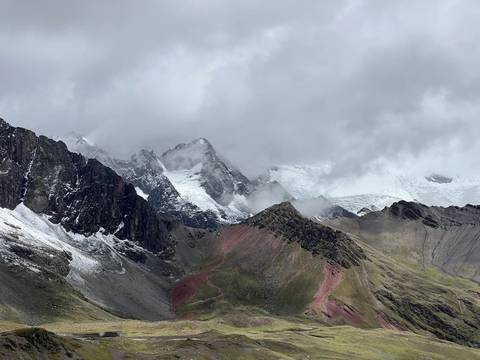       Snow-dusted Andean peaks rise dramatically with mist curling around the ridges near Rainbow Mountain.
  