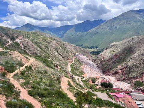       A sweeping canyon view shows the extensive white salt pans of Maras contrasting with red rock walls and green valley.
  