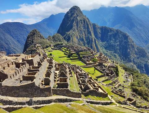      Iconic panoramic view of Machu Picchu's stone ruins perched on a ridge with Huayna Picchu towering behind.
  