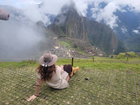       A traveler lounges on the grass gazing at Machu Picchu as clouds swirl around the mountain citadel.
  