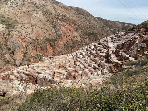       Tiered salt ponds cascade down a red rock ravine at Maras under a clear sky.
  