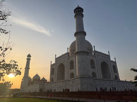       Side view of the Taj Mahal’s marble mausoleum and minarets lit by the warm glow of a setting sun.
  