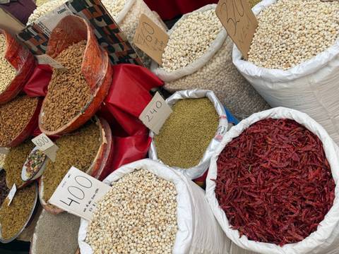       Colorful market stall with sacks of spices, dried chilies, pulses and nuts marked with handwritten price signs.
  