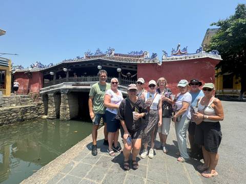       Tour group standing in front of Hoi An’s red Japanese Covered Bridge on a bright day
  