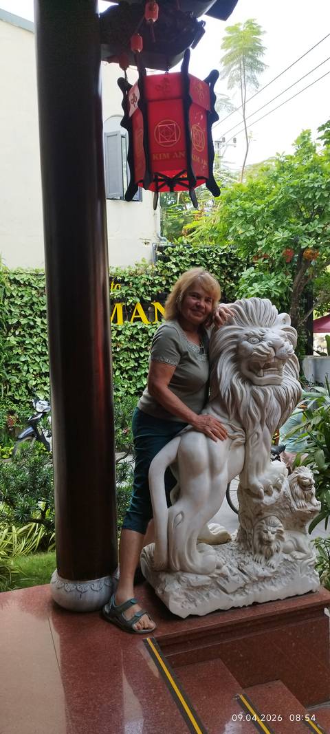       Woman posing beside a carved marble lion statue in a leafy courtyard
  