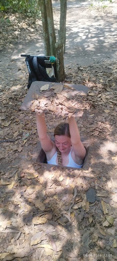       Woman emerging from a narrow Cu Chi tunnel holding a camouflaged lid above her head
  
