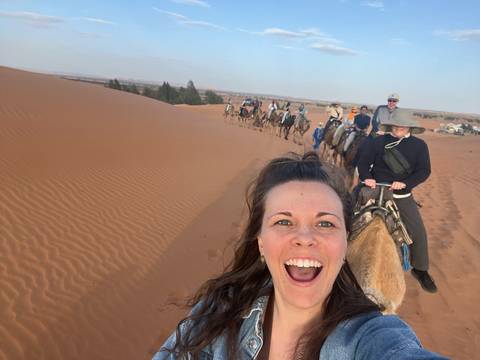       Selfie of excited traveller leading a long camel caravan across Sahara dunes
  