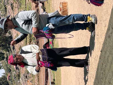       Two men in traditional attire display hand-woven pouches during an outdoor craft presentation
  