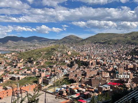       Expansive aerial view of a densely built hillside city beside a lake ringed by Andean mountains
  