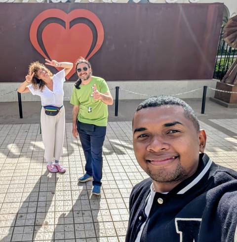       Selfie of three smiling travelers posing on a sunny paved plaza.
  