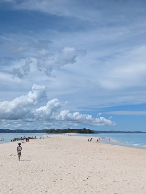       Wide view of a small green island beneath dramatic clouds and blue sky over calm ocean.
  