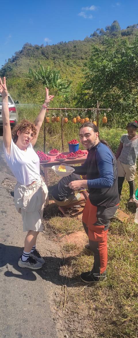       Travelers sample fruit at a roadside stall stacked with bright red berries.
  