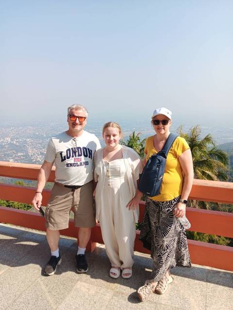       Family of three posing at mountain viewpoint above sprawling city landscape.
  