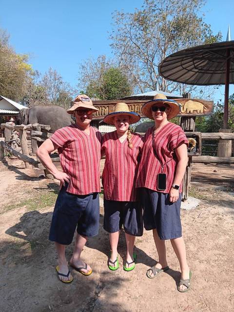       Travellers wearing traditional mahout outfits stand in front of an elephant camp enclosure.
  