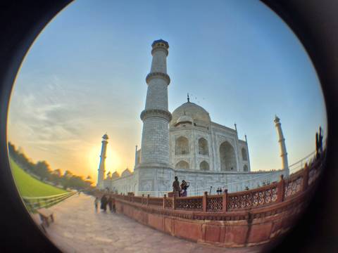       The Taj Mahal and minarets captured through a fisheye lens at sunrise with visitors in the foreground.
  