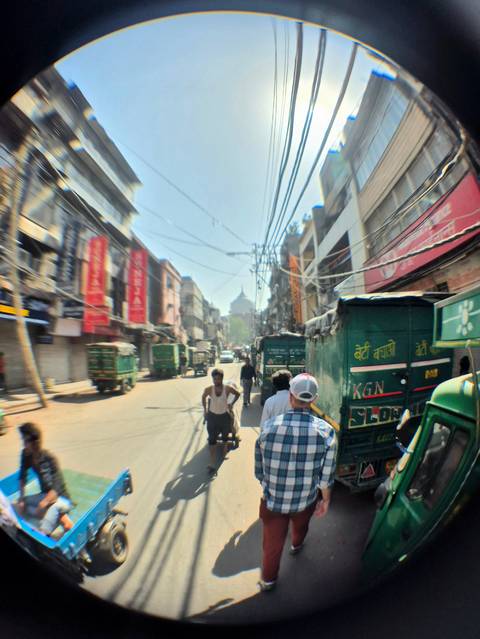       Bustling Old Delhi street with rickshaws, electric wires overhead, and distant Mughal dome visible.
  