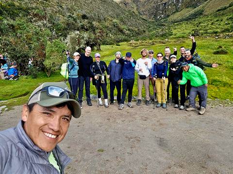       Selfie with trekking team on grassy plateau with rocky hills behind
  