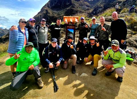       Trek group posing beside a wooden mountain sign on the Inca Trail
  